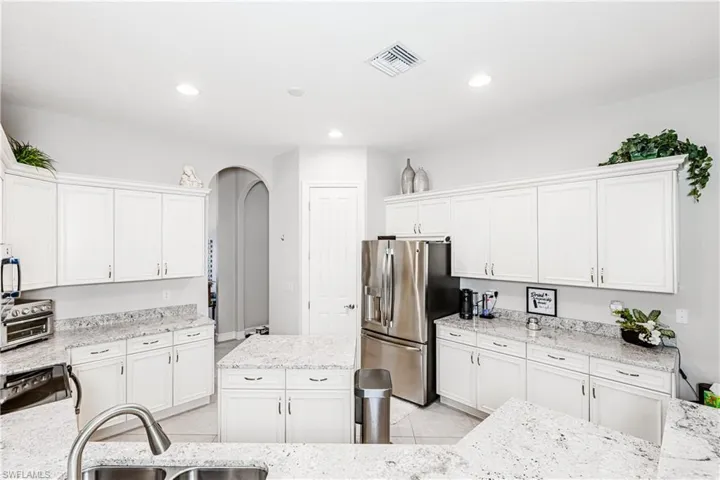 Kitchen featuring arched walkways, white cabinetry, stainless steel appliances, a kitchen island, and light tile patterned floors