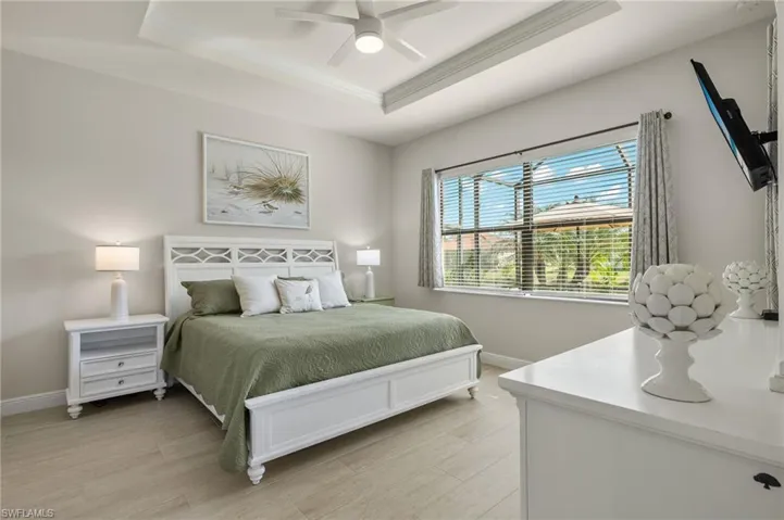 Primary Bedroom featuring tray ceiling, crown molding, ceiling fan, light tile floors, king size SLEEP NUMBER bed and peaceful water views.