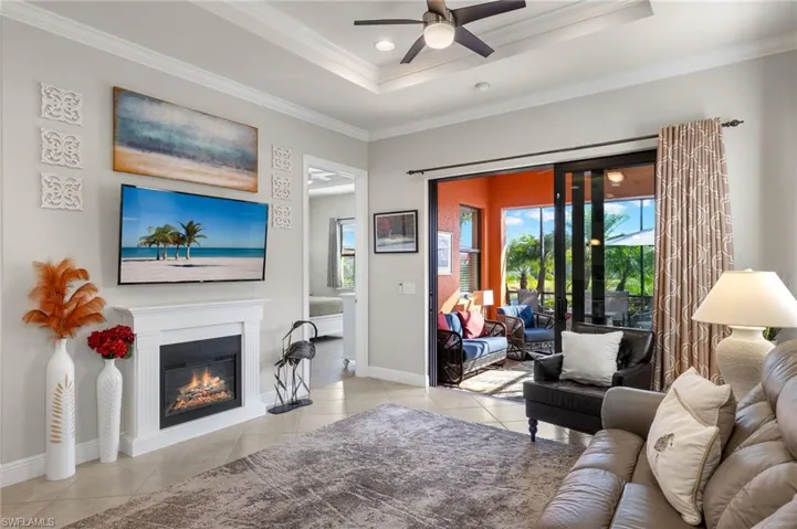 Living room with ceiling fan, tray ceiling, ornamental molding, light tile floors and fireplace.