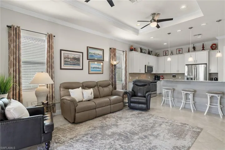 Living room with ceiling fans, tray ceiling, ornamental molding, light tile floors.