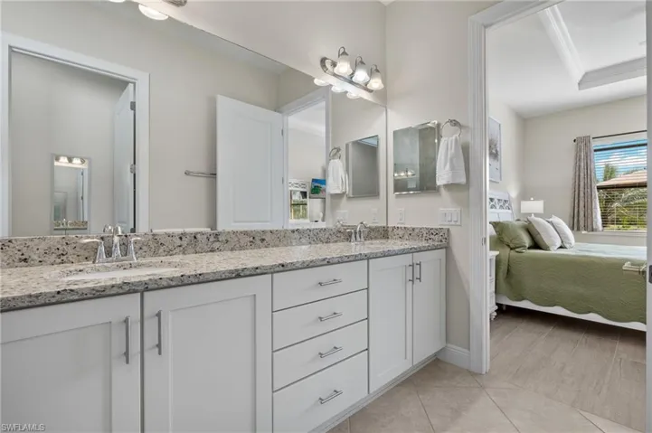 Primary bathroom with a double vanity with granite counters, light tile floors and peaceful water views.