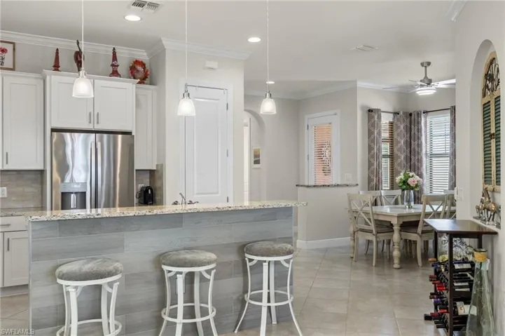 Kitchen with upgraded stainless steel appliances, an island/bar, white cabinetry, crown molding, decorative pendant light fixtures, and a pantry.