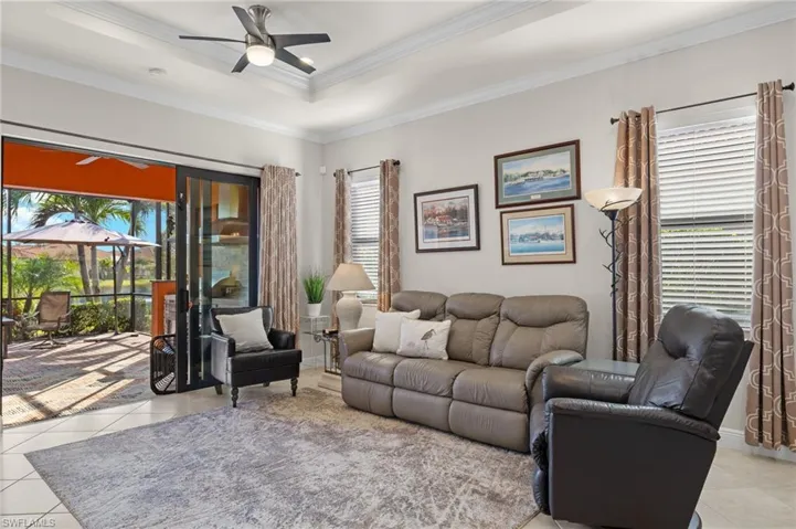 Living room with ceiling fan, tray ceiling, ornamental molding, light tile floors and tranquil water views.