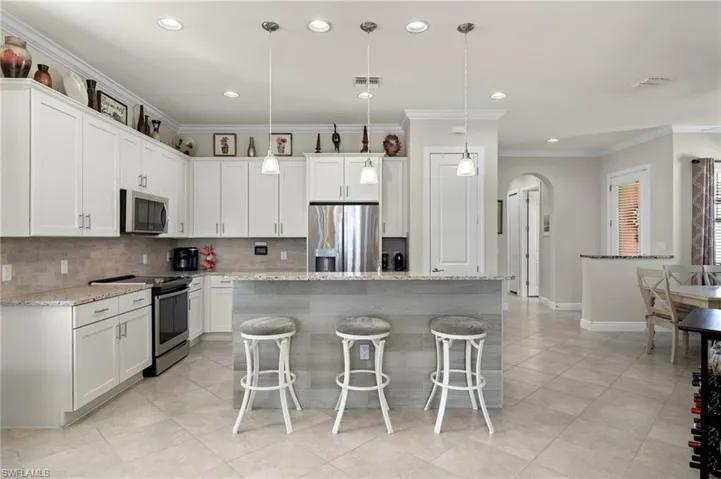 Kitchen with upgraded stainless steel appliances, a kitchen island/bar, white cabinetry, decorative pendant light fixtures, and light granite counters.