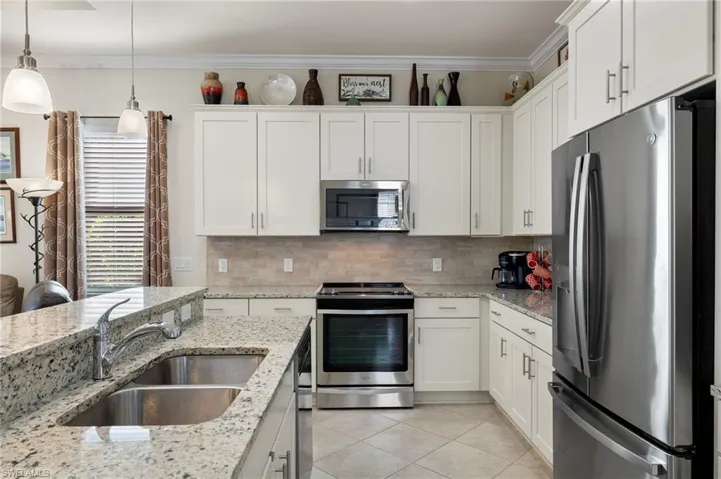 Kitchen with upgraded stainless steel appliances, an island/bar, white cabinetry, decorative pendant light fixtures, light granite counters and light tile backsplash.