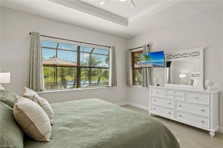 Primary Bedroom featuring tray ceiling, crown molding, ceiling fan, light tile floors, king size SLEEP NUMBER bed and tranquil water views.