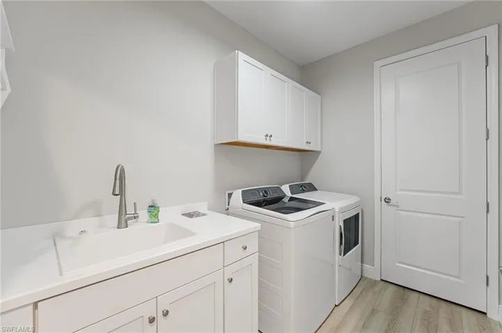 Clothes washing area with sink, light hardwood / wood-style flooring, separate washer and dryer, and cabinets