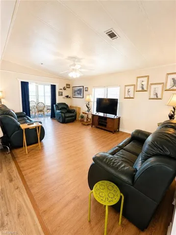 Spacious living area featuring wood-finish flooring, a ceiling fan, and ample natural light from multiple windows