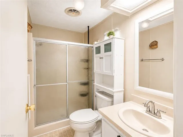 Bathroom featuring a shower with frosted sliding glass doors, a vanity with an integrated sink and light-toned countertop, and an overhead storage cabinet with glass-fronted doors