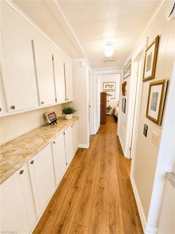 Hallway featuring extensive built-in cabinetry with white shaker-style doors, a marble-patterned countertop, and wood-finish flooring