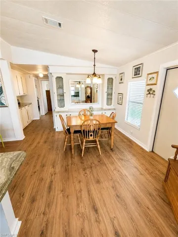 Dining area featuring wood-finish flooring, a built-in buffet with glass-front cabinetry, a central chandelier, and a window with blinds