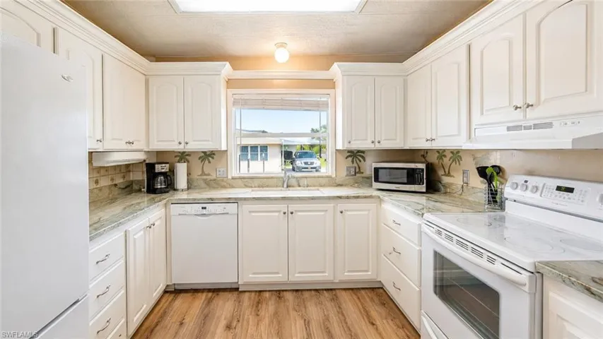 U-shaped kitchen featuring white cabinetry, light countertops, wood-finish flooring, a built-in dishwasher, and a window above the sink