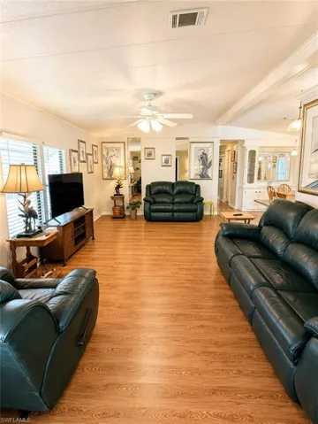 Spacious living area featuring wood-finish flooring, ample natural light from multiple windows, and a ceiling fan for comfort
