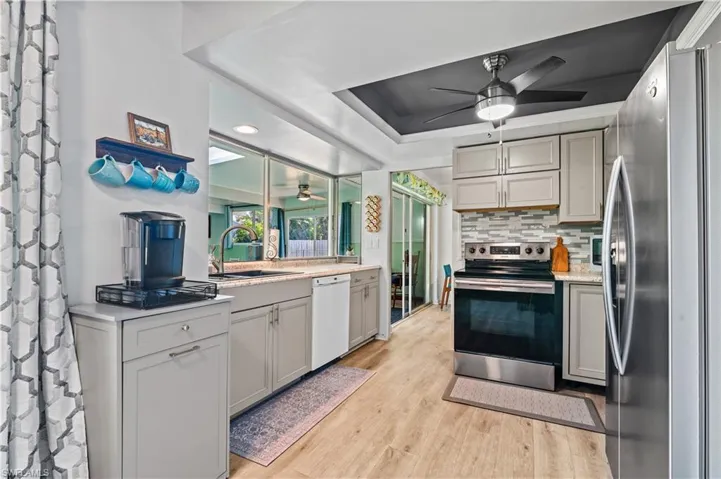 Kitchen featuring stainless steel appliances, gray cabinetry, a ceiling fan, a tray ceiling, and recessed lighting