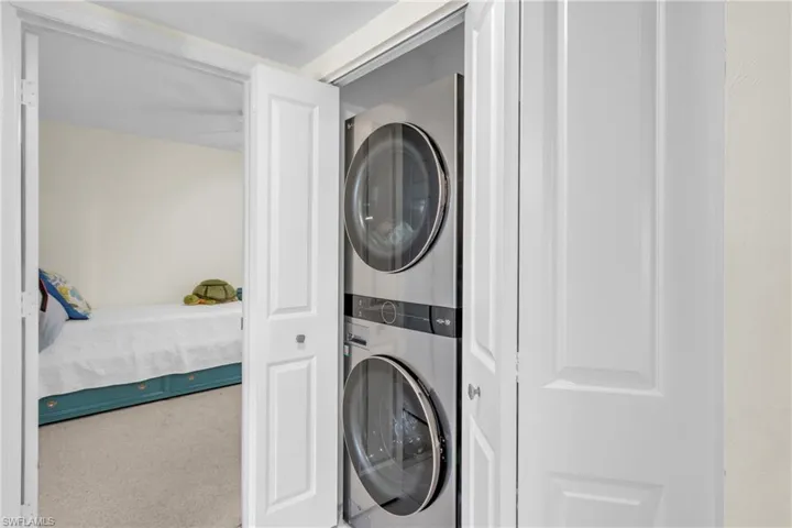 Dedicated laundry room featuring stacked washer and dryer units with modern digital controls and sleek stainless steel finishes