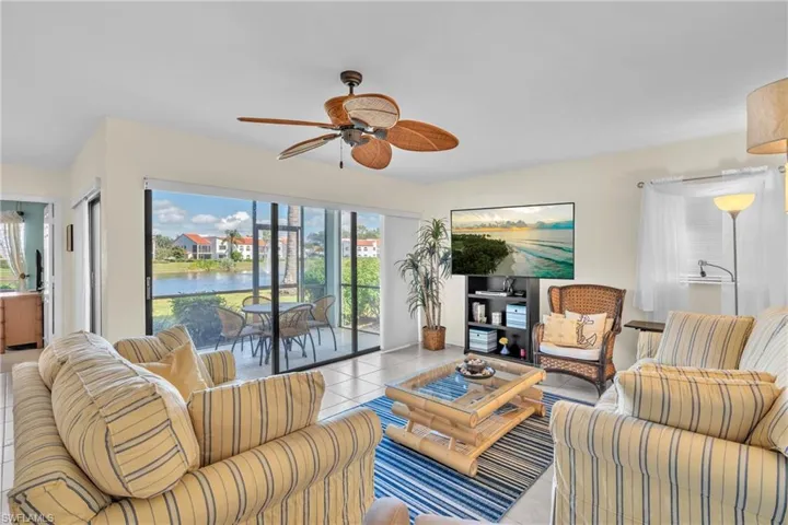 Bright, open living area showcasing striped upholstered seating, wood-finish flooring, and a ceiling fan with integrated lighting