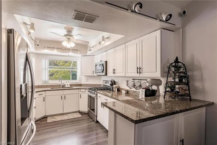 Kitchen featuring appliances with stainless steel finishes, kitchen peninsula, sink, ceiling fan, and a raised ceiling
