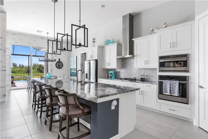 Kitchen featuring stainless steel appliances, backsplash, an island with sink, light tile patterned flooring, and wall chimney exhaust hood