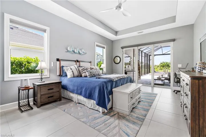 Tiled bedroom with a raised ceiling, access to outside, and ceiling fan