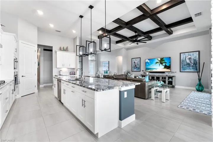 Kitchen with beamed ceiling, hanging light fixtures, an island with sink, white cabinetry, and coffered ceiling