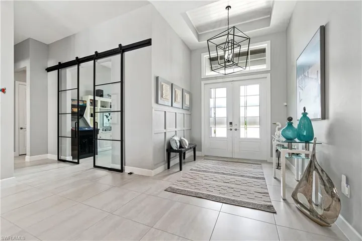 Entrance foyer with french doors, a chandelier, light tile patterned floors, a barn door, and a raised ceiling