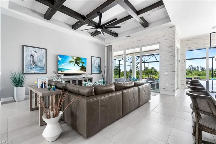 Tiled living room featuring beamed ceiling, brick wall, coffered ceiling, and ceiling fan