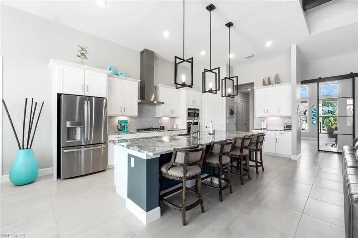 Kitchen with tasteful backsplash, appliances with stainless steel finishes, a center island with sink, and wall chimney range hood