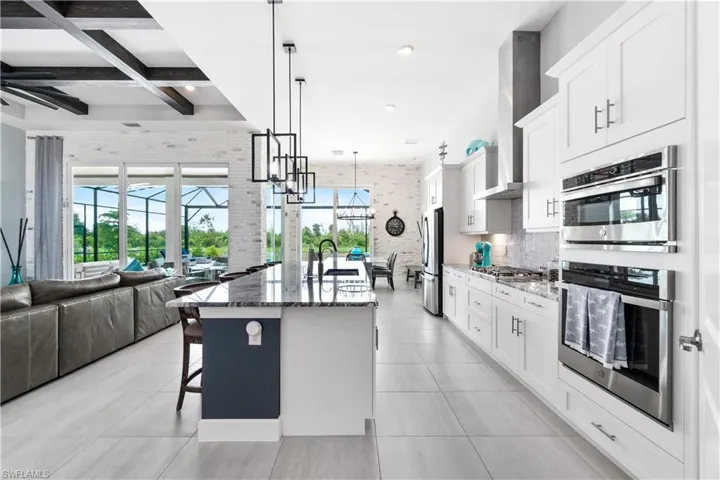 Kitchen with appliances with stainless steel finishes, beam ceiling, an island with sink, dark stone countertops, and coffered ceiling