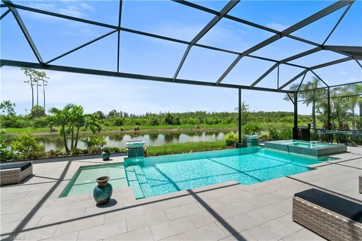 View of pool with an in ground hot tub, a water view, glass enclosure, and a patio area