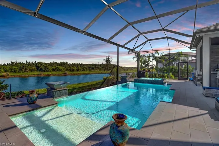 Pool at dusk with an in ground hot tub, a patio, and a lanai