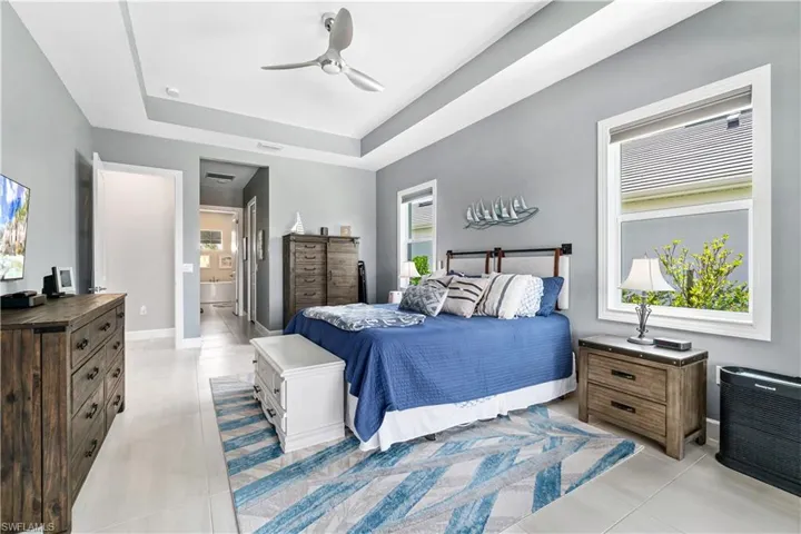 Tiled bedroom with multiple windows, ensuite bathroom, ceiling fan, and a raised ceiling