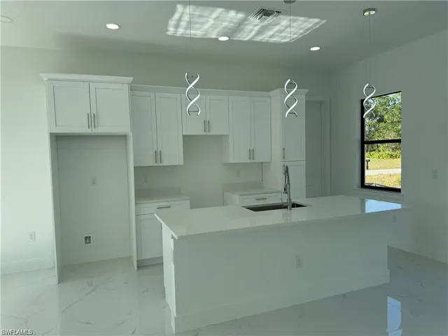 Kitchen with decorative light fixtures, sink, white cabinetry, and a kitchen island with sink