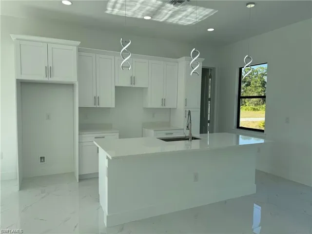Kitchen featuring white cabinetry, sink, light stone countertops, pendant lighting, and a kitchen island with sink