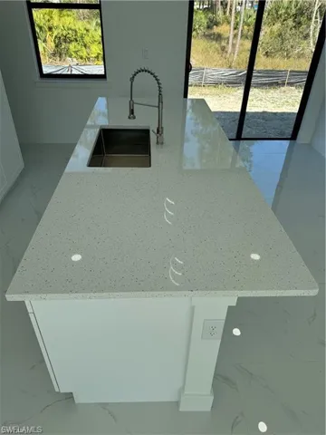 Kitchen featuring white cabinetry, light stone counters, a kitchen island, and sink