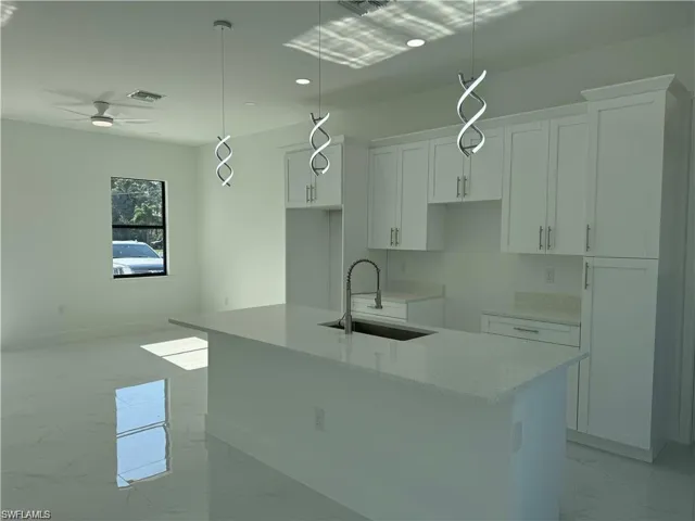 Kitchen with a kitchen island with sink, sink, and hanging light fixtures