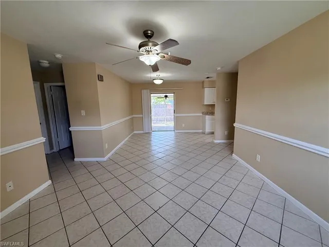 Tiled flooring throughout, neutral paint tones, ceiling fan with integrated lighting, chair rail molding, and a sliding glass door providing exterior access