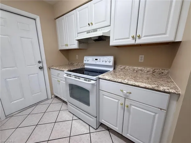 White cabinetry with gold-tone hardware, textured countertops, and a full-size range