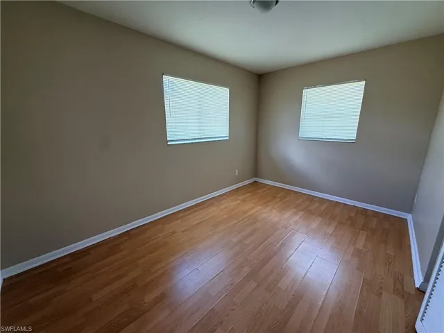 Wood-finish flooring, neutral wall paint, two windows with blinds, and a ceiling-mounted light fixture