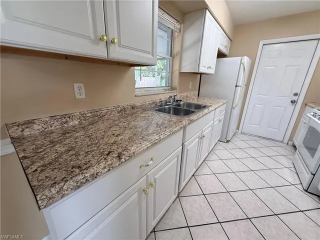 White cabinetry with gold-tone hardware, a double basin stainless steel sink, and a patterned countertop