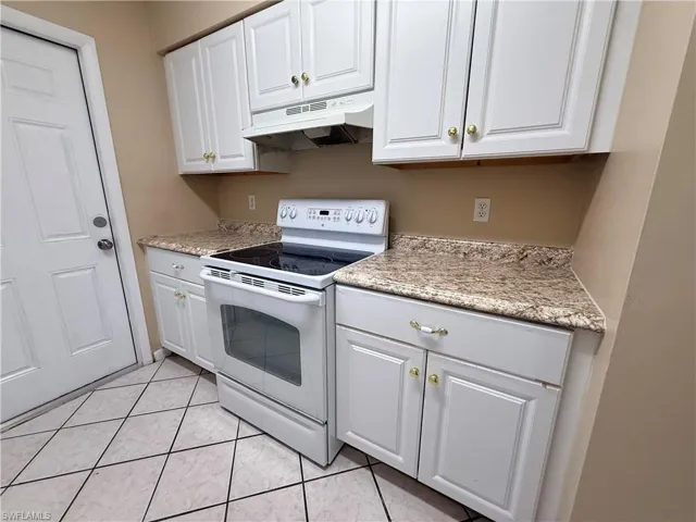 White cabinetry with gold-tone hardware, speckled countertops, and a white electric range with overhead exhaust