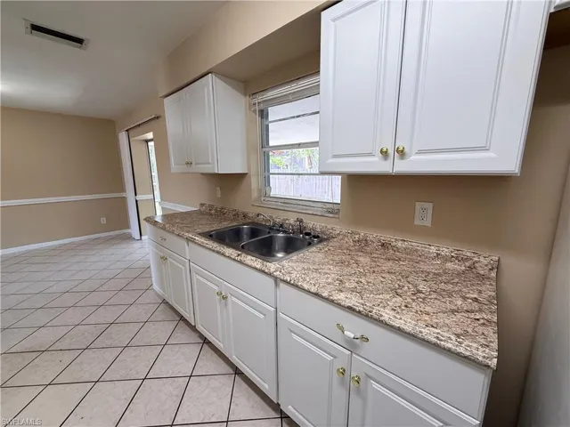 Dual basin sink with a chrome faucet, white cabinetry with gold-tone hardware, and patterned countertop
