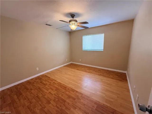 Wood-finish flooring, neutral wall tones, ceiling fan with integrated lighting, and a single window with blinds