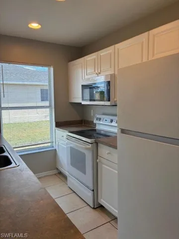Kitchen with white appliances, dark countertops, light tile patterned floors, white cabinetry, and recessed lighting