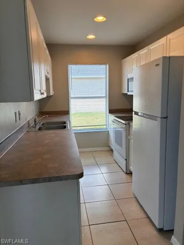 Kitchen with dark countertops, refrigerator, light tile patterned floors, stove, and white cabinetry