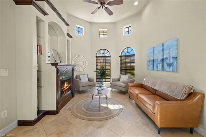 Living area featuring ceiling fan, baseboards, a lit fireplace, a towering ceiling, and recessed lighting