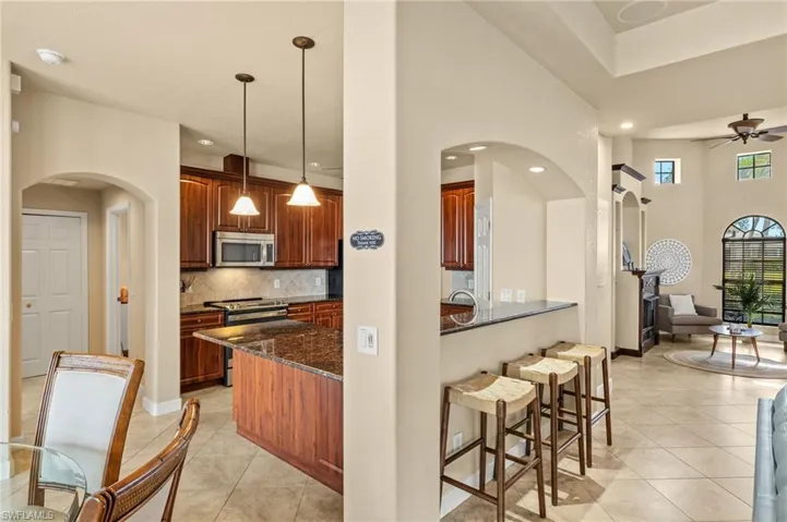 Kitchen with appliances with stainless steel finishes, dark stone countertops, arched walkways, a kitchen bar, and a ceiling fan