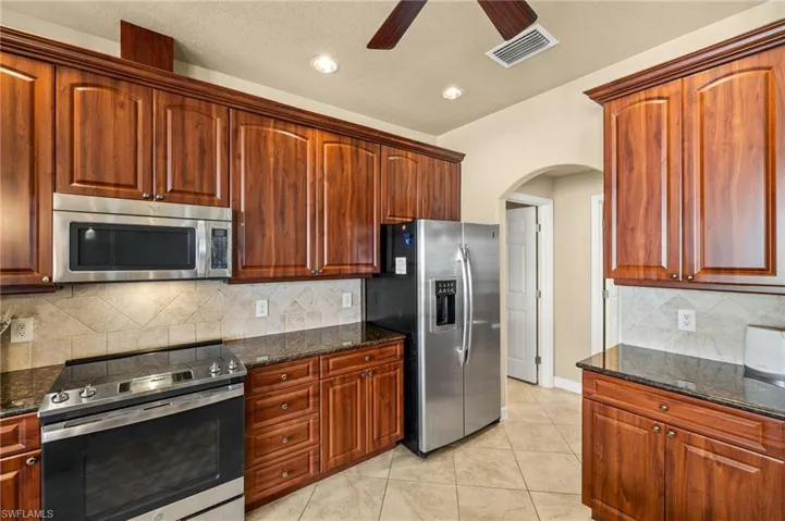Kitchen featuring stainless steel appliances, arched walkways, dark stone countertops, ceiling fan, and backsplash