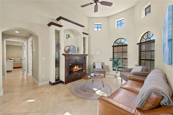 Living room with ceiling fan, a fireplace, arched walkways, baseboards, and a towering ceiling