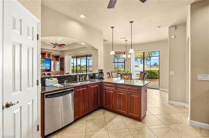 Kitchen featuring stainless steel dishwasher, a ceiling fan, a sink, dark stone countertops, and a textured ceiling