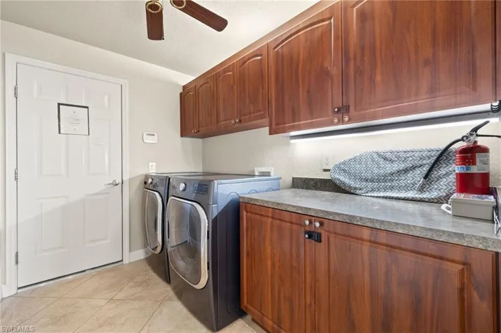 Washroom with cabinet space, washing machine and clothes dryer, ceiling fan, light tile patterned floors, and baseboards